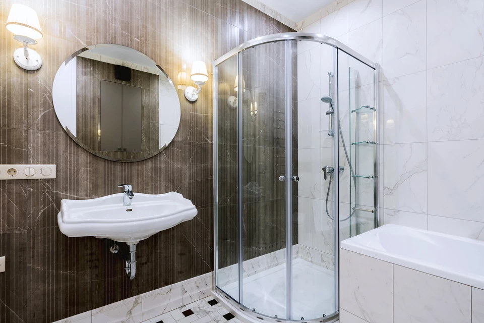 Salle de bain moderne avec douche à l'italienne vitrée, lavabo suspendu blanc, miroir circulaire et baignoire d'angle